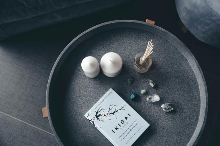 Photo of a candle, natural stones and a book on Ikigai placed on a grey marble tray, against a black-grey background.